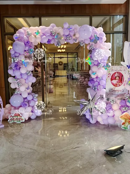 A whimsical fairy and butterfly themed entrance arch. The structure is covered in shades of purple and silver balloons, with butterfly cutouts and mushroom props adding to the enchanted forest feel.
