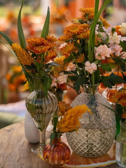 Close-up of a table centerpiece. The arrangement includes orange flowers in textured glass vases, adding a touch of elegance to the rustic theme.