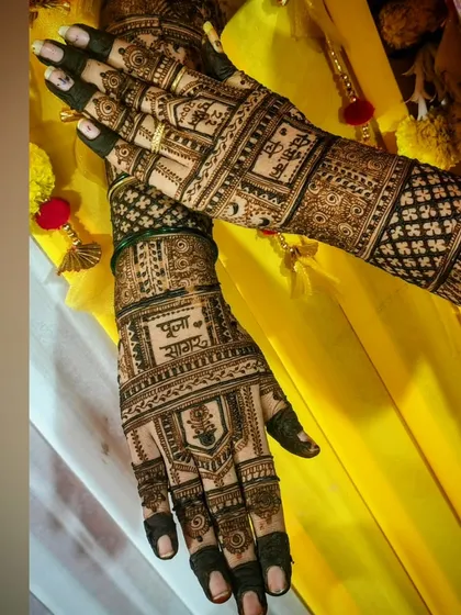 The complete view of Pooja's bridal mehendi. The names 'Pooja' and 'Sagar' are beautifully integrated into the intricate design, set against a vibrant yellow backdrop from her ceremony.