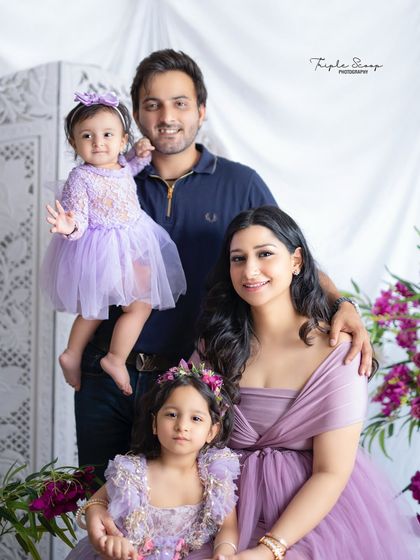 A beautiful family portrait with coordinating lavender outfits. The floral arrangement in the background adds a lovely touch of color.
