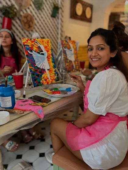 A participant smiling as she works on her colorful ballerina painting. The cafe workshops have a lively and social atmosphere.