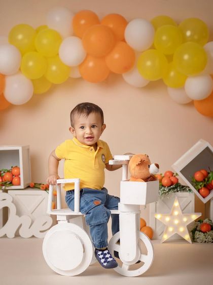 This little boy is having a great time riding his toy bicycle during his fun, orange-themed first birthday shoot.