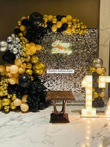 A 17th birthday setup featuring a silver sequin wall, a black and gold organic balloon garland, and light-up marquee numbers.