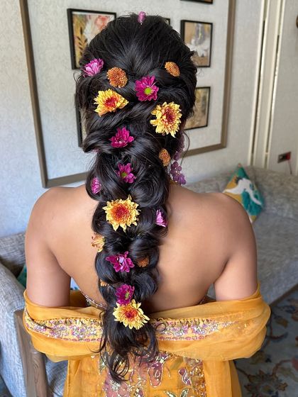 A detailed back view of the Haldi braid, showing the rich texture of the hair and the generous placement of fresh, multi-colored flowers.