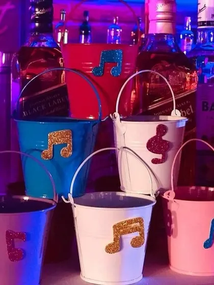 Colorful mini buckets decorated with glittery musical notes. These fun containers can be used to serve drinks or hold snacks, adding another layer of thematic detail to the retro party.