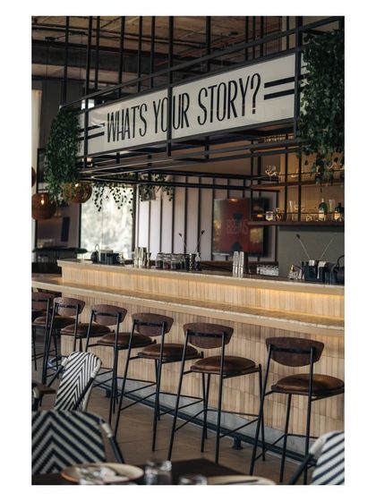 A side view of the bar, highlighting the clean lines of the bar stools and the prominent placement of the brand's tagline. The industrial grid above frames the entire scene.