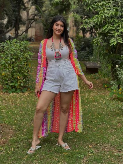 This Holi-inspired outfit features an all-white base of a tank top and shorts, brought to life with a vibrant, colorful shrug. The tribal-style necklace adds an extra layer of festive fun.