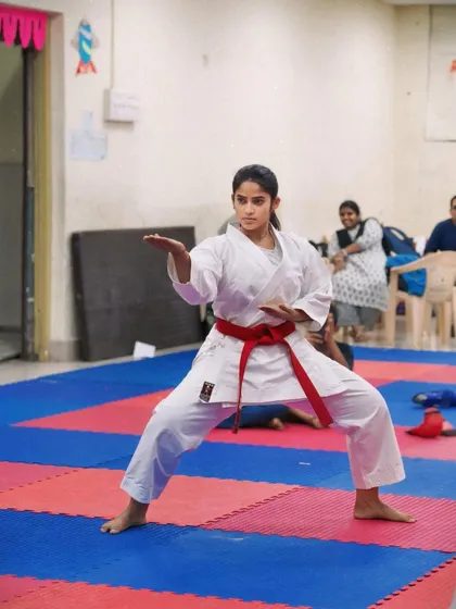 A student demonstrates a classic karate pose, her red belt indicating an advanced level of skill. Her form is a result of years of dedicated practice.