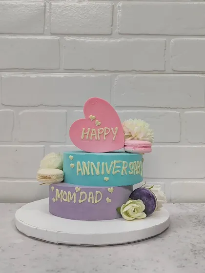 A sweet and simple anniversary cake for Mom and Dad. This two-tiered pastel cake is adorned with fresh flowers, macarons, and a heart topper to celebrate their love.