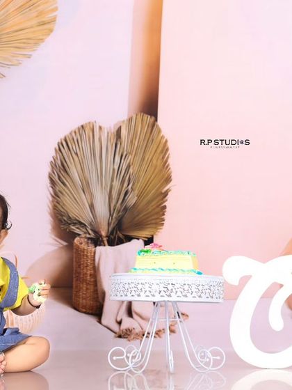 A sweet moment as the birthday girl sits beside her cake, ready to celebrate. The "One" sign and modern balloon arch complete this stylish first birthday setup.