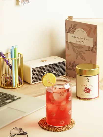 A cozy desk setup featuring a glass of floral iced tea, a journal, and a laptop, creating a scene of mindful work or relaxation.