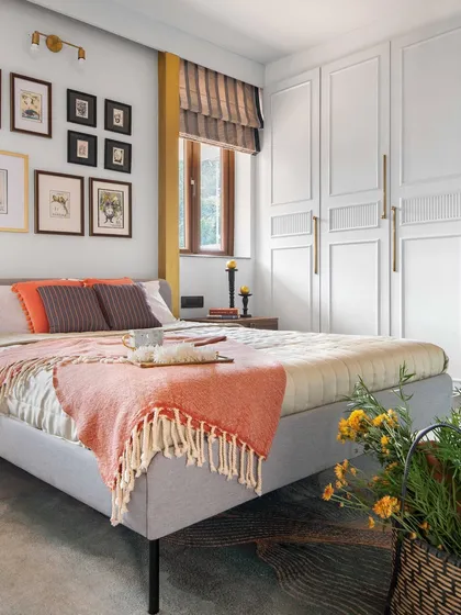 This bedroom is a study in texture and warmth. The upholstered bed is set against a wall of framed botanical prints, while the custom white wardrobe with clean lines provides ample storage without overwhelming the serene space.