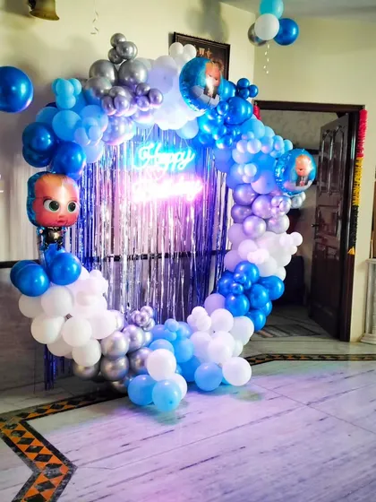 A full view of the Boss Baby themed balloon ring with a silver fringe backdrop and neon sign, perfect for a fun and modern birthday party at home.