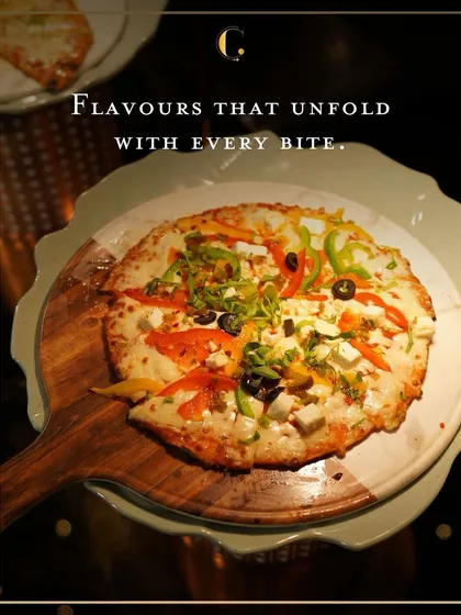 A colourful vegetarian pizza topped with bell peppers, olives, and paneer, presented on a modern serving board. This dish from our live pizza station is a feast of flavours.