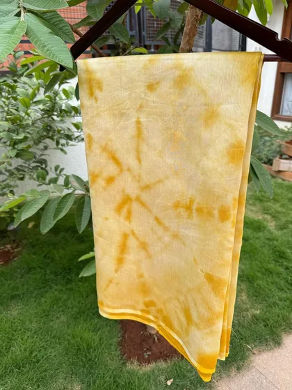 A beautiful marigold-dyed saree hanging in the garden. The tie-dye pattern creates a stunning starburst effect in a vibrant yellow hue.