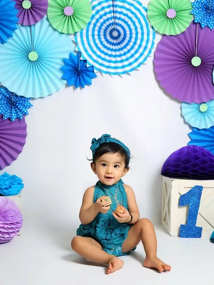 A solo portrait of the little girl from the twin session. The vibrant backdrop of paper fans in shades of blue and purple creates a stunning visual.