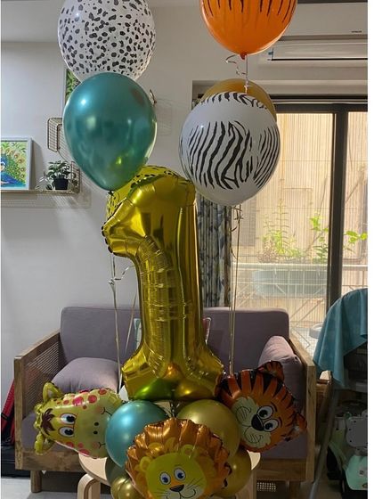 A jungle-themed balloon bouquet for a first birthday. This arrangement includes a large gold number "1" foil, along with zebra-print, tiger-print, and animal-shaped balloons for a wild celebration.