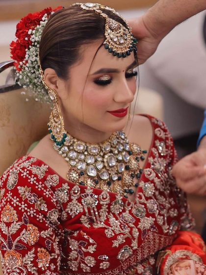 Final touches on the hair. A traditional bun adorned with flowers is the perfect hairstyle for this classic red lehenga look.