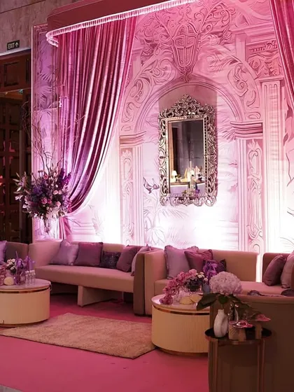 The soft pink lighting enhances the elegance of this lounge setup, with its curved sofas, rich purple cushions, and beautifully detailed architectural backdrop.