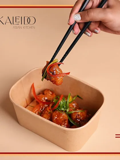 A single bite of a vegetarian dish held by chopsticks over a delivery container. This shows that you can enjoy an exquisite Asian meal even when you're going veggie.