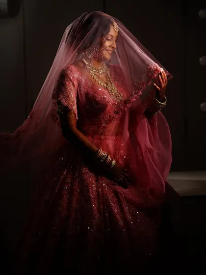 A full-length shot capturing the graceful movement of the bride's veil. The dramatic lighting highlights the rich color of her lehenga and the flawless finish of her makeup.
