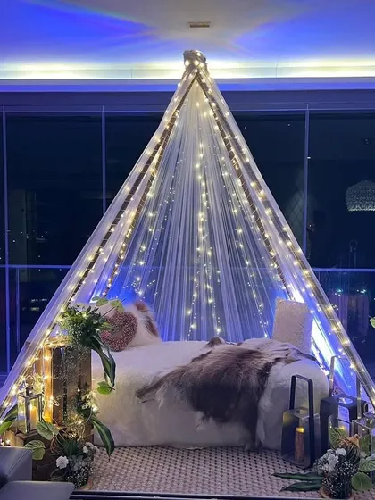 We transformed a simple balcony into a romantic boho-themed escape for an anniversary. This cozy teepee, draped in fairy lights and surrounded by rustic floral arrangements, creates a perfect intimate setting against the city lights.