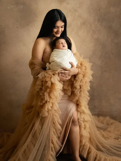 A candid moment of a mother smiling as she holds her baby. The flowing gown adds a touch of elegance and drama to the portrait.