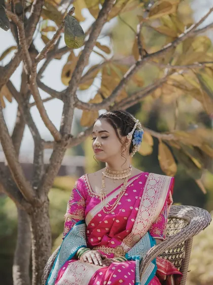A serene portrait of a bride in a pink and blue Paithani. Her makeup is soft and romantic, with braided hair details and fresh flowers adding a touch of whimsy.