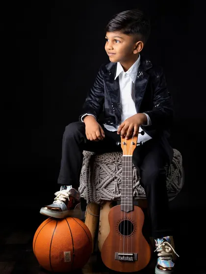 A stylish shot of the young boy in a black velvet jacket, posing with both a basketball and a ukulele.