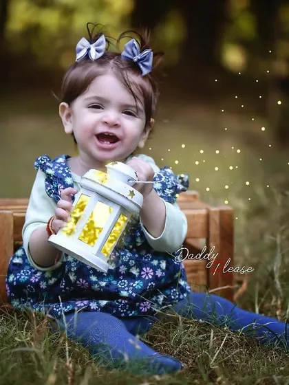 A magical outdoor portrait of a one year old girl sitting in the grass and holding a glowing lantern. The added sparkle effect makes the photo even more special.