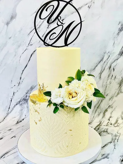 For a classic and romantic wedding, I created this elegant two-tier buttercream cake. The design features a subtle textured pattern on the bottom tier, touches of gold leaf, and a beautiful arrangement of fresh white roses and carnations, all topped with a custom "Y&N" monogram.