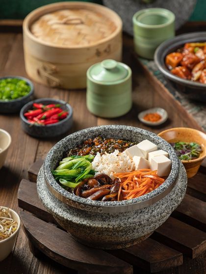 A wider view of the vegetarian stone bowl from YouMee, showing the accompanying condiments and steamer baskets.