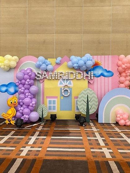A full view of a different Peppa Pig stage, with Peppa's house as the centerpiece, surrounded by balloon clouds, trees, and character props.