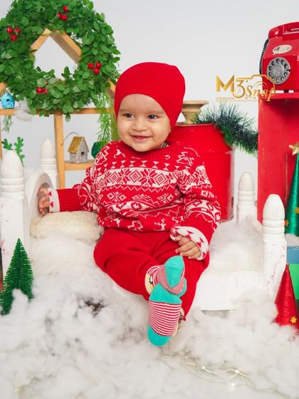 Another look from our Christmas mini-sessions. This baby is wearing a cozy winter sweater, sitting on a sleigh prop in a cheerful red and white holiday setup.
