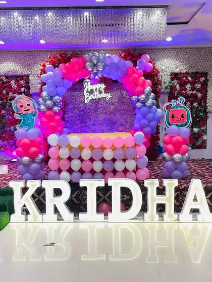 A wide shot of the Cocomelon birthday stage for Kridha, showcasing the entire setup with the '1' marquee number and balloon pillars.