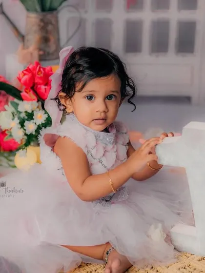Posing with the number '1' to mark her special day. The soft colors and floral background create a beautiful setting for a first birthday.