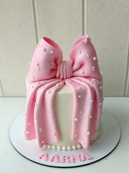 An elegant and chic bow cake, featuring a smooth white base and an oversized, handcrafted pink fondant bow studded with delicate pearls.