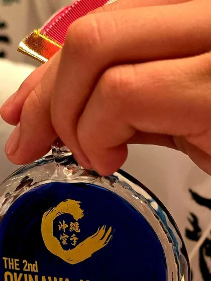 A close up shot of a student's hand holding their medal from the Okinawa World Junior Tournament. This represents the tangible reward for their immense effort and training.