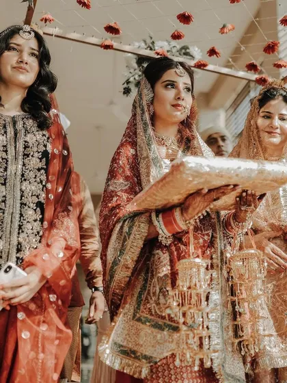 A bride participates in a wedding ritual, holding a decorated pillow, surrounded by her family.