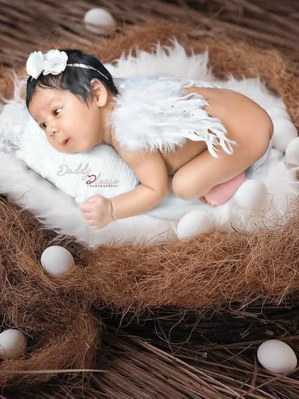 A creative newborn photo with the baby posed with small angel wings, resting in a cozy nest prop surrounded by decorative eggs. This is a beautiful way to capture their angelic look.
