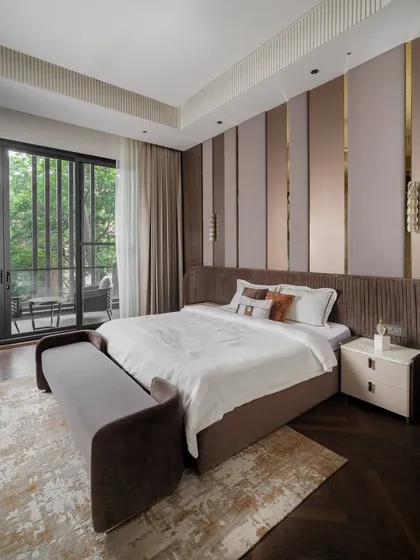 A bedroom designed as a warm, inviting retreat. The feature wall behind the bed combines upholstered panels with sleek metallic accents. A custom fluted headboard and bespoke bench at the foot of the bed complete the look.