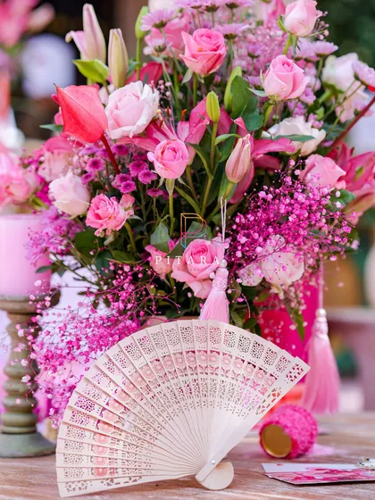 A beautiful lace fan rests against a lush bouquet of pink lilies and roses, with a tassel detail adding a touch of elegance. This is how we layer textures and elements to create a rich visual story.