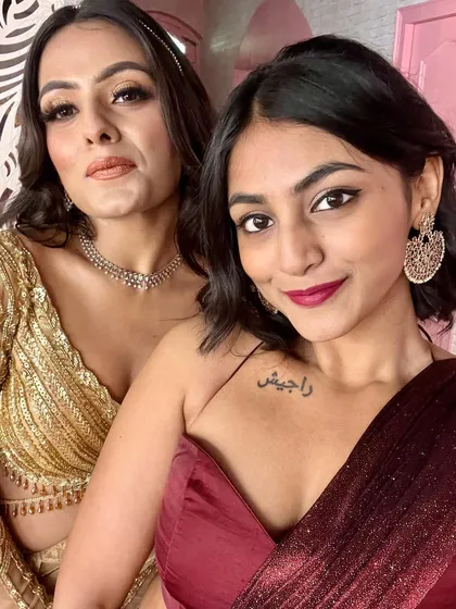 A selfie with a friend, both of us in our wedding best. I'm wearing a deep maroon draped gown, while she is in a glamorous gold sequined outfit.