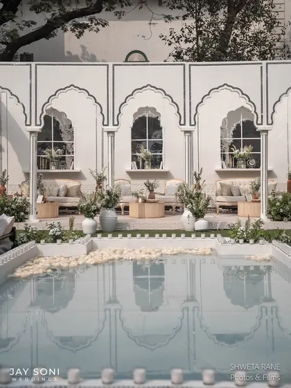 A serene poolside lounge area, where the reflection of the white arched pavilion in the water adds another layer of beauty to the scene.
