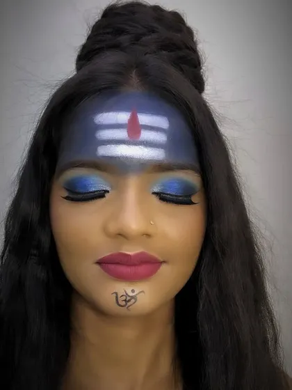 This full-face view shows the modern interpretation of a Shiva-inspired look, combining traditional elements with contemporary makeup techniques like a sharp lip and a small Om tattoo design.