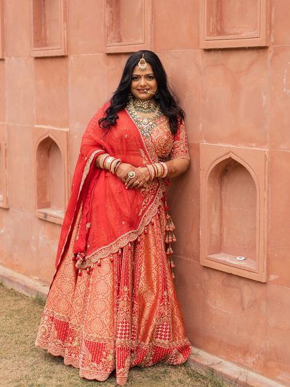 The bride, Nirzari, standing against the iconic architectural niches of Jaisalmer, her red lehenga a stunning statement of bridal beauty.