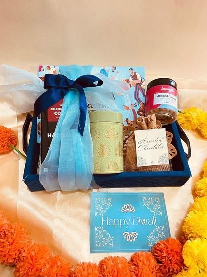 A blue tray hamper filled with coffee, cookies, and chocolates, elegantly wrapped in blue tulle.