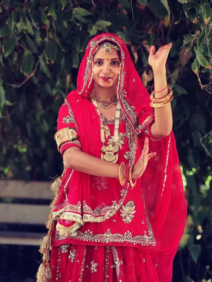 The traditional Rajasthani poshak is a story in itself. This vibrant red attire, with its intricate details and bold jewelry, is not just a costume. It is a symbol of our heritage, and wearing it feels like I am carrying the legacy of my ancestors with every step.