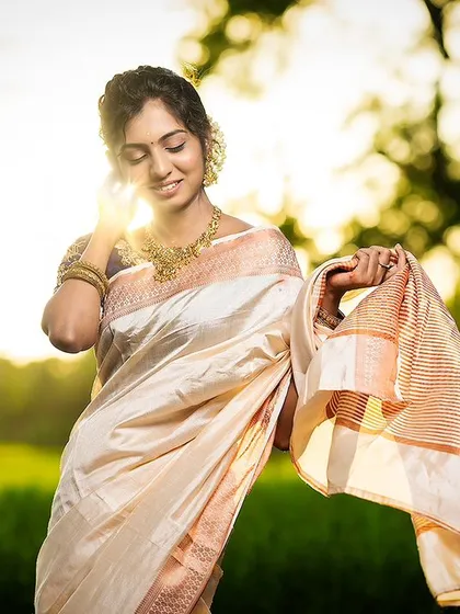 Get the perfect festive look for Onam or any traditional function with our elegant off-white saree. The golden hour lighting in this shot highlights the beautiful texture of the fabric and the rich navy blue aari work blouse.