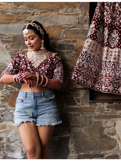 A modern and confident bridal portrait. The bride pairs her traditional blouse and jewelry with denim shorts, showcasing her unique style before the ceremony.